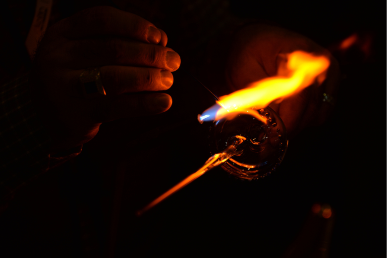Hands holding a piece of glass heated by blowtorch.