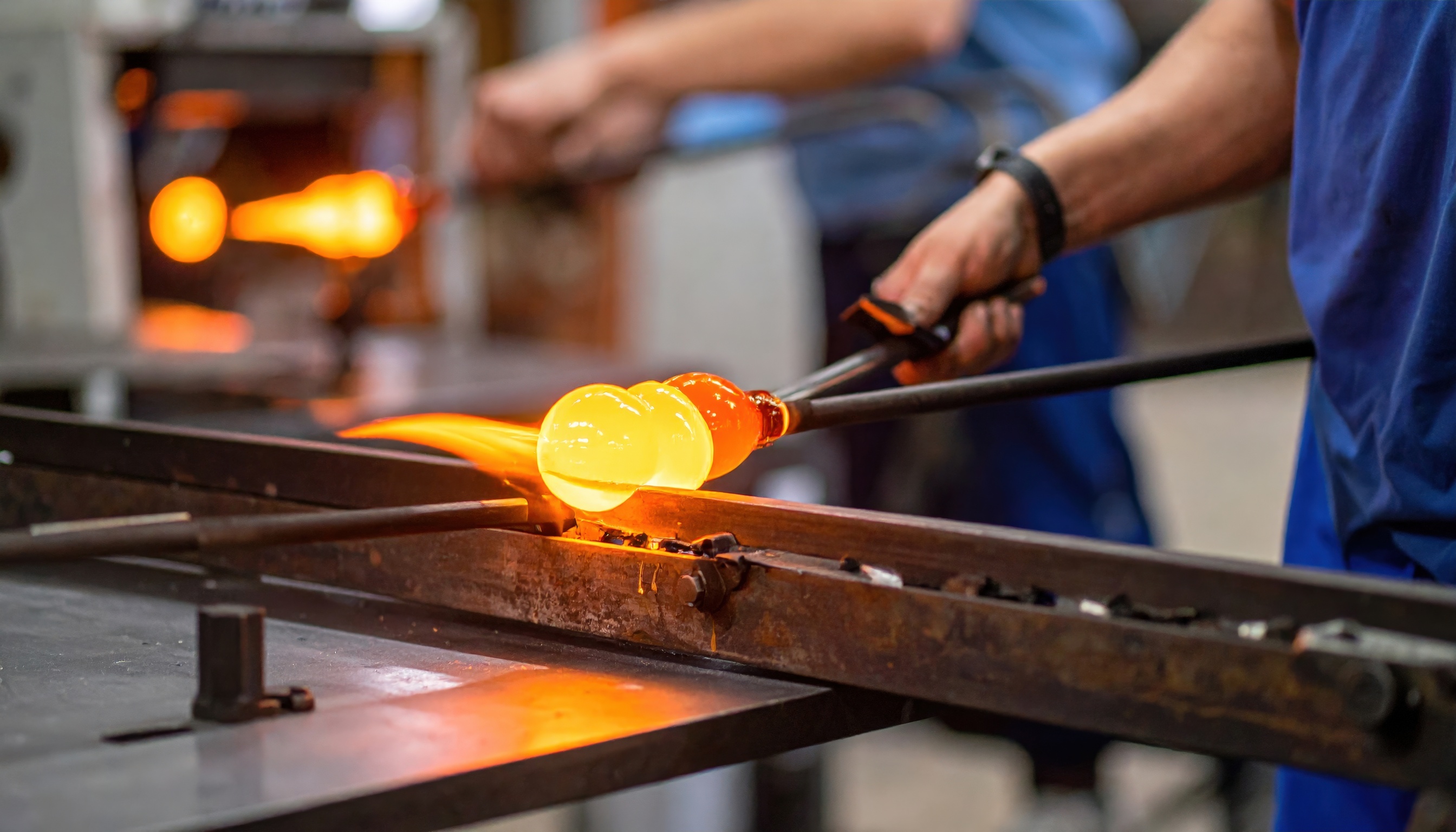 Molten glass being shaped on a metal bench.